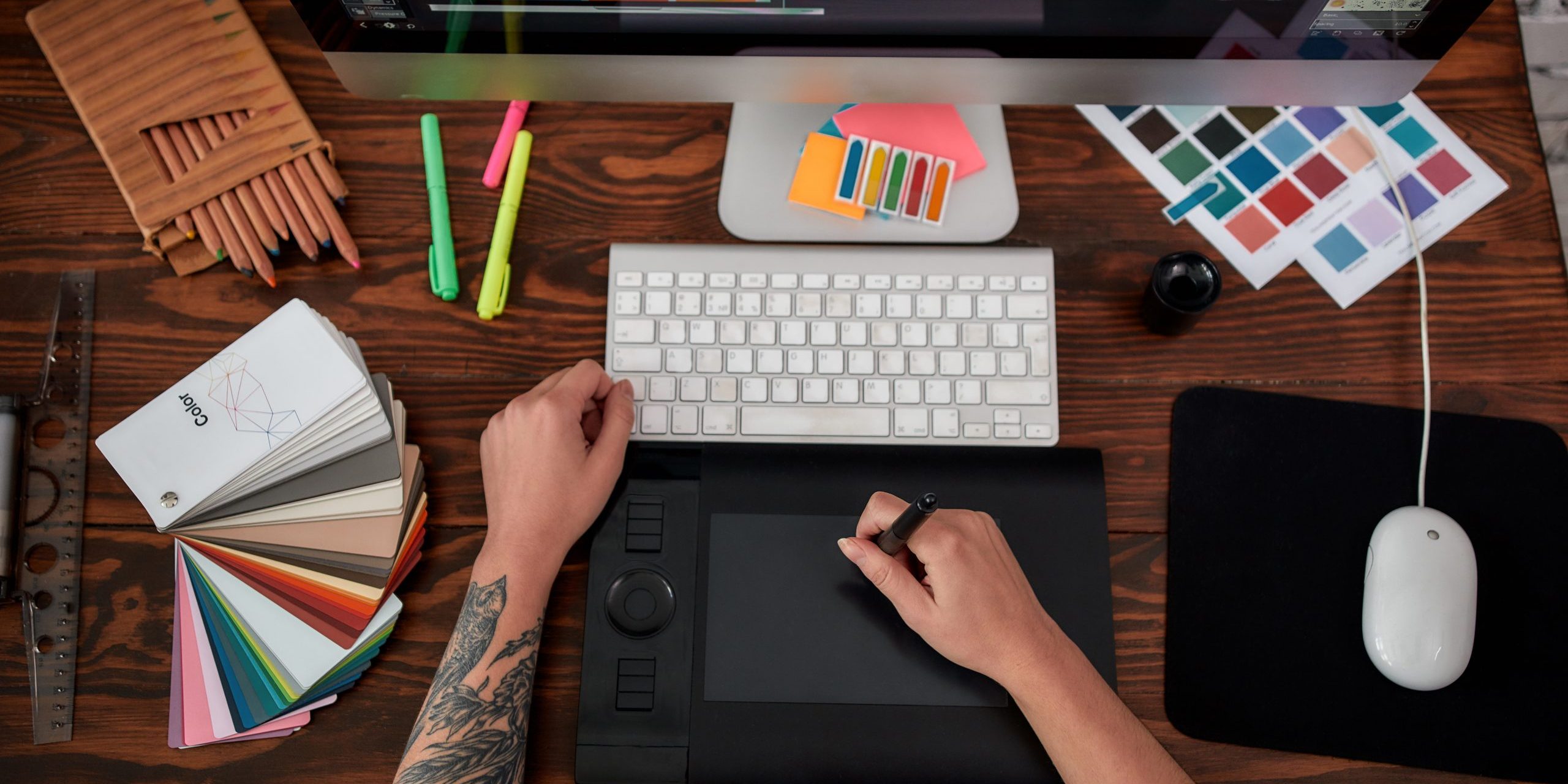 Professional web illustrator. Top view of a graphic designer using graphic tablet and computer in the office or studio. Workplace with graphic tablet, keyboard, computer and color swatches
